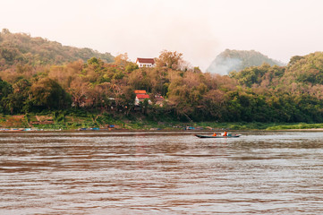 Luang Prabang, Laos - Row boat with monks in Mekong river with mountain temple