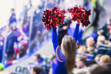 Female cheerleader in red blue uniform with pom-pom with audience in the background performing and...