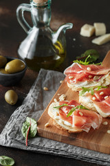 Traditional parma cured ham antipasto. Bruschetta set with Parma Ham and Parmesan Cheese. Small sandwiches with prosciutto, parmesan cheese, fresh arugula, olives and pine nuts