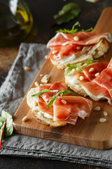 Traditional parma cured ham antipasto. Bruschetta set with Parma Ham and Parmesan Cheese. Small sandwiches with prosciutto, parmesan cheese, fresh arugula, olives and pine nuts