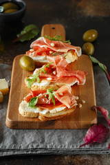 Traditional parma cured ham antipasto. Bruschetta set with Parma Ham and Parmesan Cheese. Small sandwiches with prosciutto, parmesan cheese, fresh arugula, olives and pine nuts
