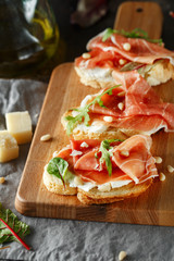 Traditional parma cured ham antipasto. Bruschetta set with Parma Ham and Parmesan Cheese. Small sandwiches with prosciutto, parmesan cheese, fresh arugula, olives and pine nuts