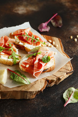 Traditional parma cured ham antipasto. Bruschetta set with Parma Ham and Parmesan Cheese. Small sandwiches with prosciutto, parmesan cheese, fresh arugula, olives and pine nuts