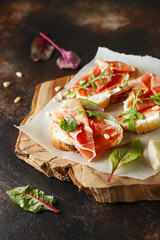 Traditional parma cured ham antipasto. Bruschetta set with Parma Ham and Parmesan Cheese. Small sandwiches with prosciutto, parmesan cheese, fresh arugula, olives and pine nuts