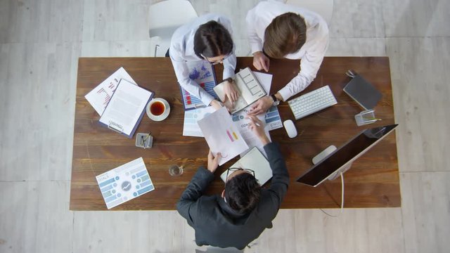 Directly above shot of business attorney in suit and young businesspeople sitting at table and discussing documents