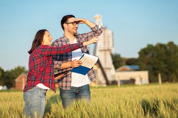 Happy young female and male agronomists or farmers inspecting wheat fields before the harvest....