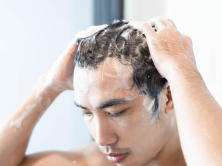 Naklejka premium Closeup young man washing hair with with shampoo in the bathroom, health care concept, selective focus