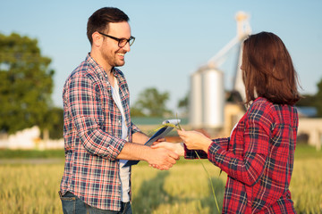 Two happy young female and male farmers or agronomists shaking hands after inspection of a wheat...