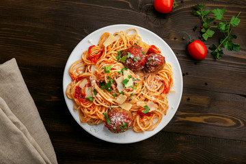 Plate of spaghetti with meatballs, parmesan and tomato sauce on a rustic wooden table. Tasty Italian pasta food. Top view shot directly above.