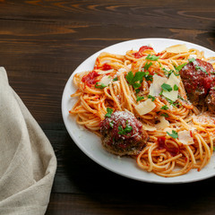 Pasta with meatballs, parmesan and tomato sauce on a plate.  Homemade Italian spaghetti on a rustic wooden table.