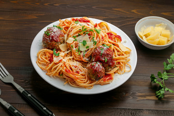 Plate of spaghetti with meatballs, parmesan and tomato sauce on a rustic wooden table. Tasty Italian pasta food.