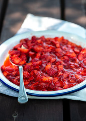 Strawberry jam in an enamel plate on a wooden garden table. Vegan dessert, healthy lifestyle.