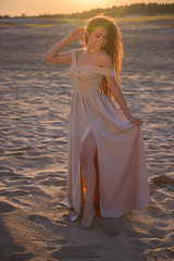 Fototapeta na wymiar Brunette girl in an evening dress in the desert at sunset