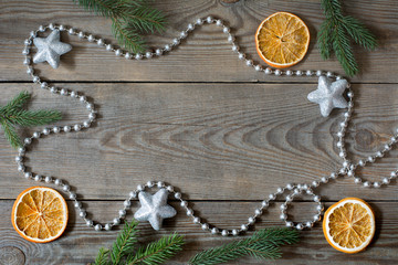 Christmas composition with silver bead chain, brocade stars, orange slices and fir tree branches on wooden background