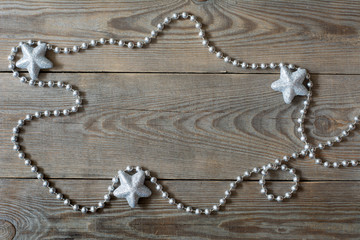 Christmas card concept with bead chain and three silver glitter stars on wooden background - deep shadows, text space