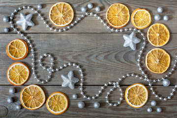 Christmas composition with silver bead chain, brocade stars and balls, and orange slices on wooden background - deep shadows