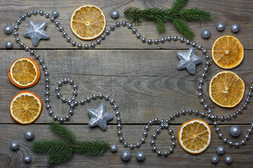 Christmas composition with silver bead chain, brocade stars and balls, orange slices and two fir tree branches on wooden background