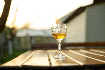 A glass of cognac is standing on a wooden table outside at sunset on a summer evening. Strong drinks. Close up.