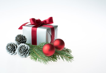 Christmas composition with a gift wrapped with red ribbon, silver cones, red baubles and a fir tree branch - isolated on white background