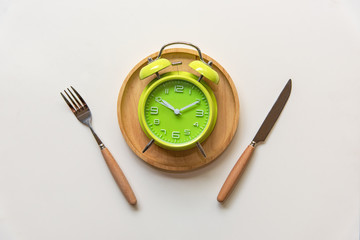 Diet and weight loss for healthy intermittent fasting lunchtime . Alarm clock and plate with cutlery on concrete background. Diet and Healthy Concept