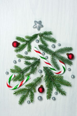 Christmas tree concept with green fir tree branches, glitter globules, red baubles and candy canes on white background