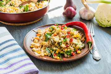 Veggie fried rice with cabbage, carrots, corn, onion, beans and pepper with chopped parsley and chili in a plate on a wooden table, fork and napkin rustic style - Indian and Asian cuisine