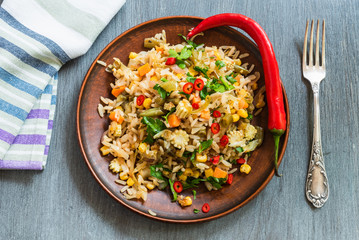 Veggie fried rice with cabbage, carrots, corn, onion, beans and pepper with chopped parsley and chili in a plate on a wooden table, fork and napkin rustic style - Indian and Asian cuisine