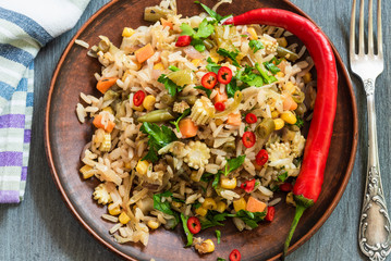 Veggie fried rice with cabbage, carrots, corn, onion, beans and pepper with chopped parsley and chili in a plate on a wooden table, fork and napkin rustic style - Indian and Asian cuisine