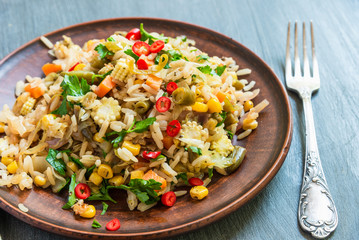 Fried vegetarian rice with carrots, corn, onions, beans and pepper with chopped parsley and chili in a plate on a wooden table close-up, top view, rustic style - a dish of Indian and Asian cuisine