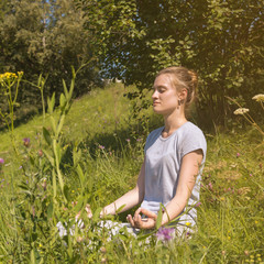 Young attractive woman sitting in lotus position in a meadow near trees - concept of rest and...