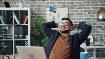 Happy young businessman relaxing in office enjoying work break smiling sitting at desk on comfortable chair dreaming. People, job and relaxation concept. - Powered by Adobe