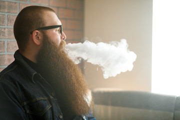Vape bearded man. An adult man with a very long beard in glasses smokes an electronic cigarette in the bar. Bad habit that is harmful to health. Vaping activity. Close up.