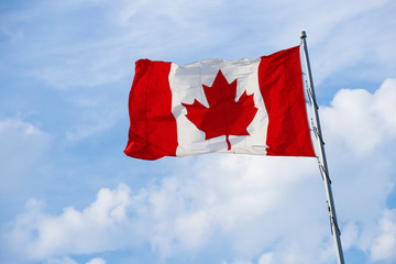 Canadian Flag on the pole blowing in the wind with clouds and blue sky. - obrazy, fototapety, plakaty