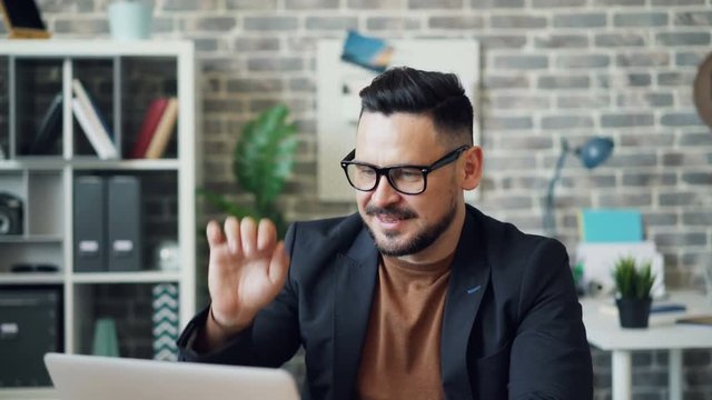 Bearded young man is working with laptop then stretching arms relaxing in office resting during work break. People, modern technology and rest concept.