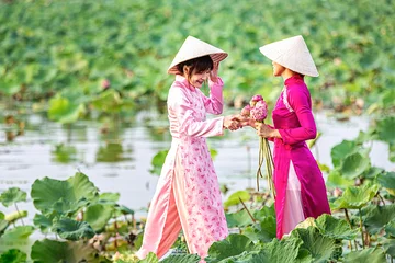 Abwaschbare Fototapete Water lilies on hand. Two Vietnamese woman on a wooden boat and collecting lotus flowers. Female boating on lakes harvest Pink Lotus flower. The flooding season there are many water lilies. © Thirawatana