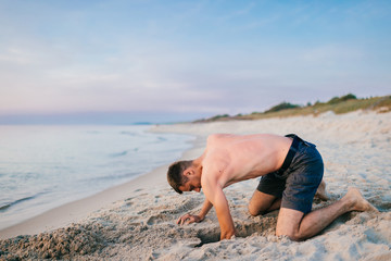 Man on the beach digging hole in sand beyond the sea in summer.