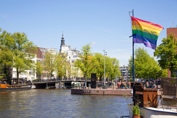 Gay pride peace rainbow flag and Amsterdam canal houses background.