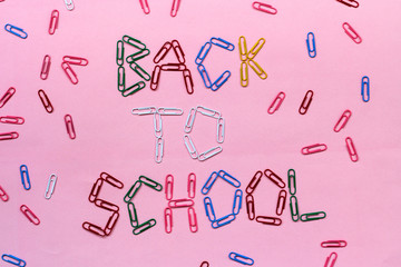 colored paper clips on a pink background lined with the inscription - back to school.