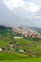 Fototapeta na wymiar Vertical photo of picturesque Sicilian village Gangi in Italy captured in fog. The small historical city is surrounded by green landscape and is located on the top of the hills. Italian countryside
