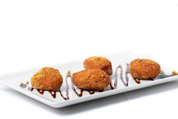 assortment of croquettes with a vinaigrette on a white rectangular plate