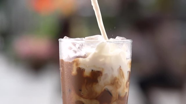 close up pouring milk to glass of ice coffee