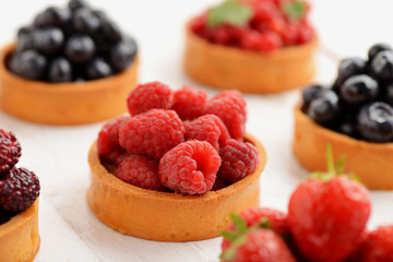Fruit and berry tartlets dessert tray assorted . Beautiful delicious tarts, bright, colorful pastry cakes sweets with fresh raspberries, figs, strawberry. on white wooden background
