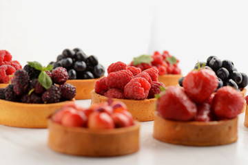 Fruit and berry tartlets dessert tray assorted . Beautiful delicious tarts, bright, colorful pastry cakes sweets with fresh raspberries, figs, strawberry. on white wooden background