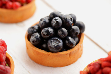 Fruit and berry tartlets dessert tray assorted . Beautiful delicious tarts, bright, colorful pastry cakes sweets with fresh raspberries, figs, strawberry. on white wooden background