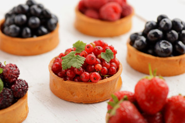 Fruit and berry tartlets dessert tray assorted . Beautiful delicious tarts, bright, colorful pastry cakes sweets with fresh raspberries, figs, strawberry. on white wooden background