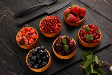 Fruit and berry tartlets dessert tray assorted . Beautiful delicious tarts, bright, colorful pastry cakes sweets with fresh raspberries, figs, strawberry. on dark wooden background