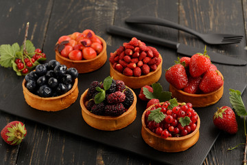 Fruit and berry tartlets dessert tray assorted . Beautiful delicious tarts, bright, colorful pastry cakes sweets with fresh raspberries, figs, strawberry. on dark wooden background