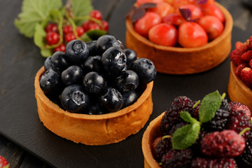 Fruit and berry tartlets dessert tray assorted . Beautiful delicious tarts, bright, colorful pastry cakes sweets with fresh raspberries, figs, strawberry. on dark wooden background