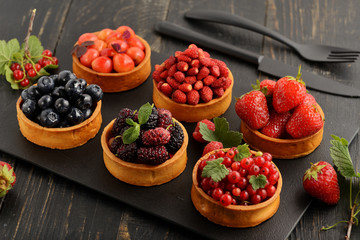 Fruit and berry tartlets dessert tray assorted . Beautiful delicious tarts, bright, colorful pastry cakes sweets with fresh raspberries, figs, strawberry. on dark wooden background