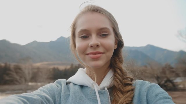 Close-up portrait. A young girl takes a selfie on camera in the open air, spinning with the camera in his hands. Attractive blonde takes himself to the camera, smiling. Point of view. Slow motion, 4K